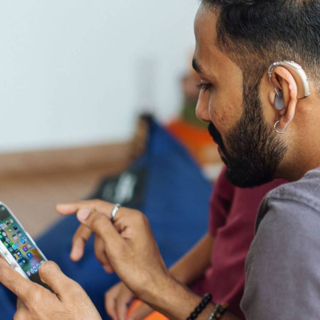 A man wearing a hearing aid holds an iPhone