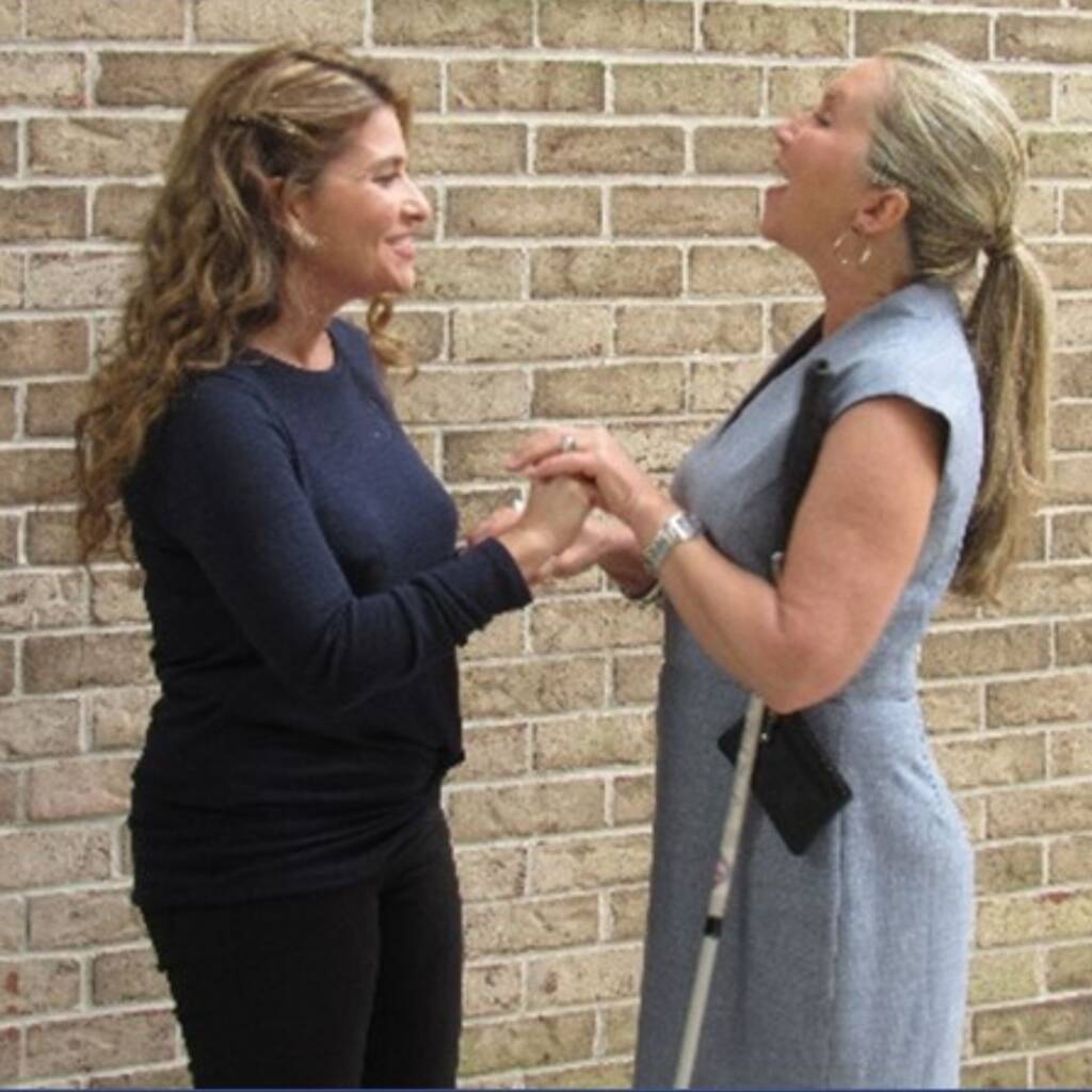 Two women touching hands while one of the women holds a white cane