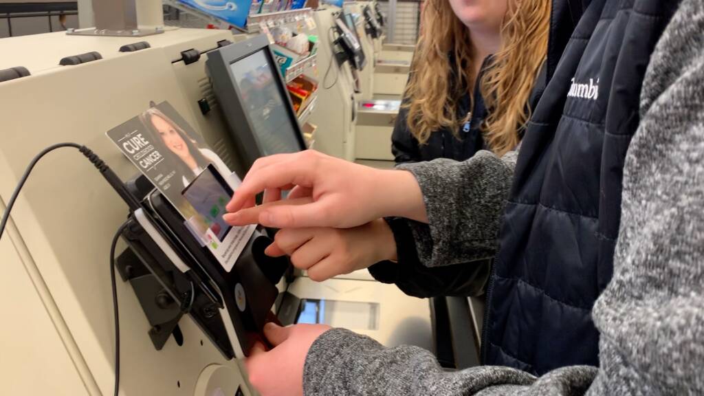 Close up of a woman guiding a man's hand to a credit card reader.