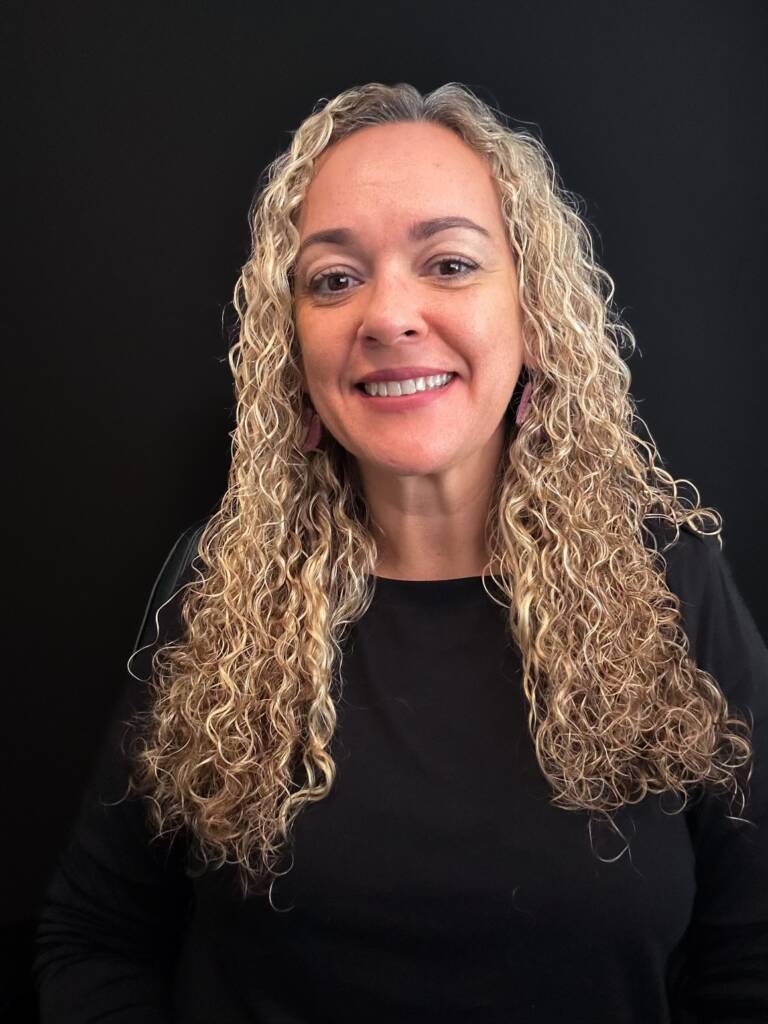 A woman with long curly blonde hair named Isabel smiles into the camera
