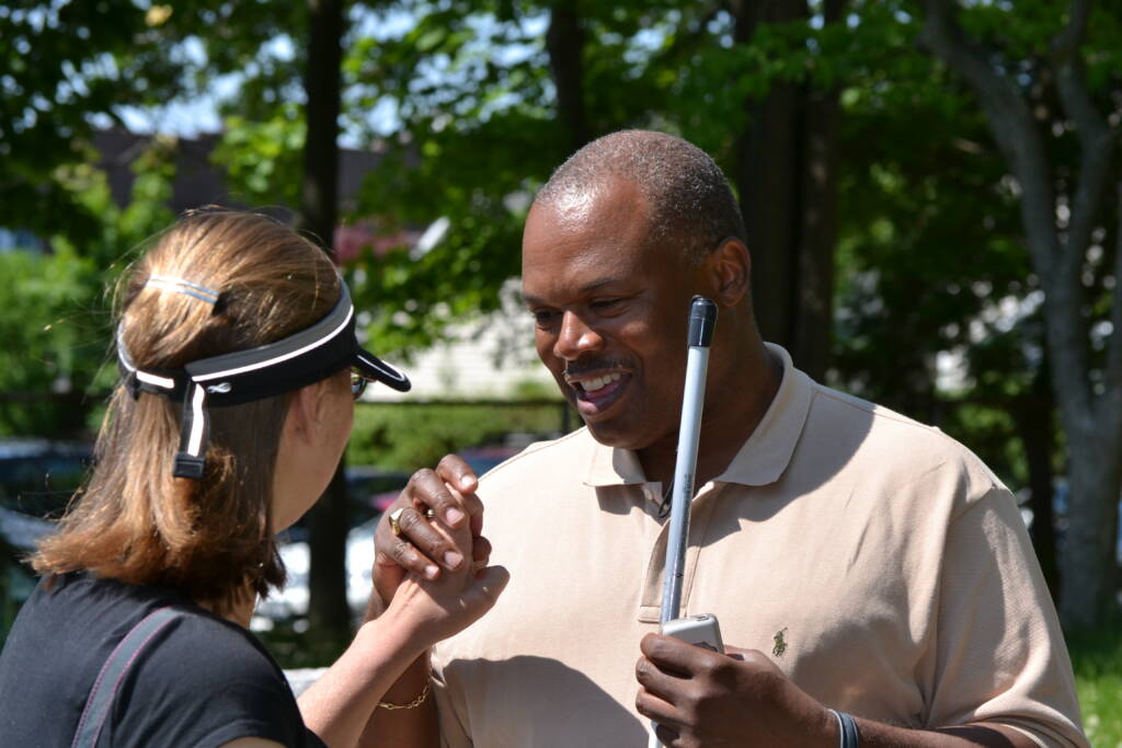 A woman and man communicate in tactile sign language while the man also holds a white cane.