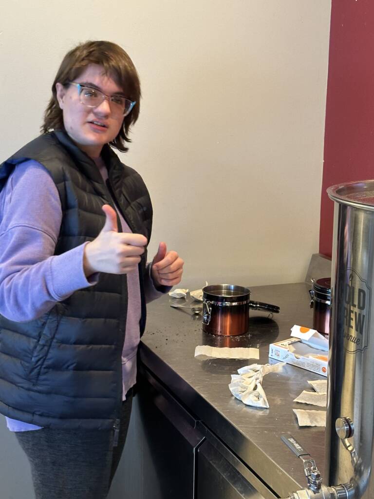 A young person does a thumbs up gesture next to a countertop that has cooking materials on it.