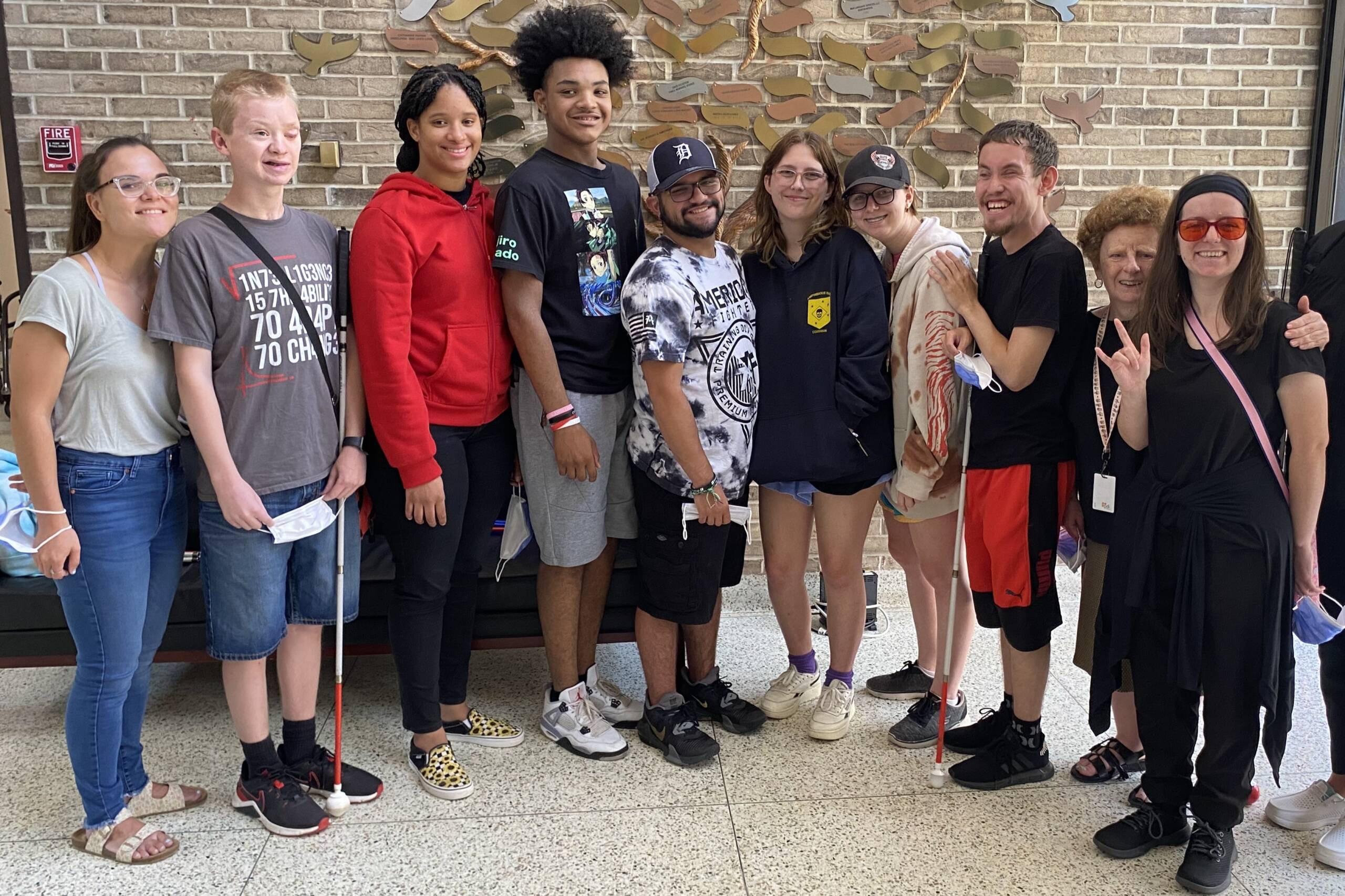 A group of youths and an older adult smiling next to each other, some holding white canes.