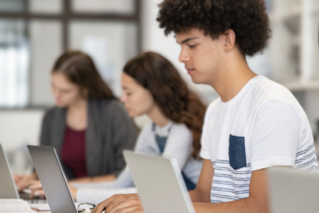 Teens sitting at a table working on their laptop computers. 