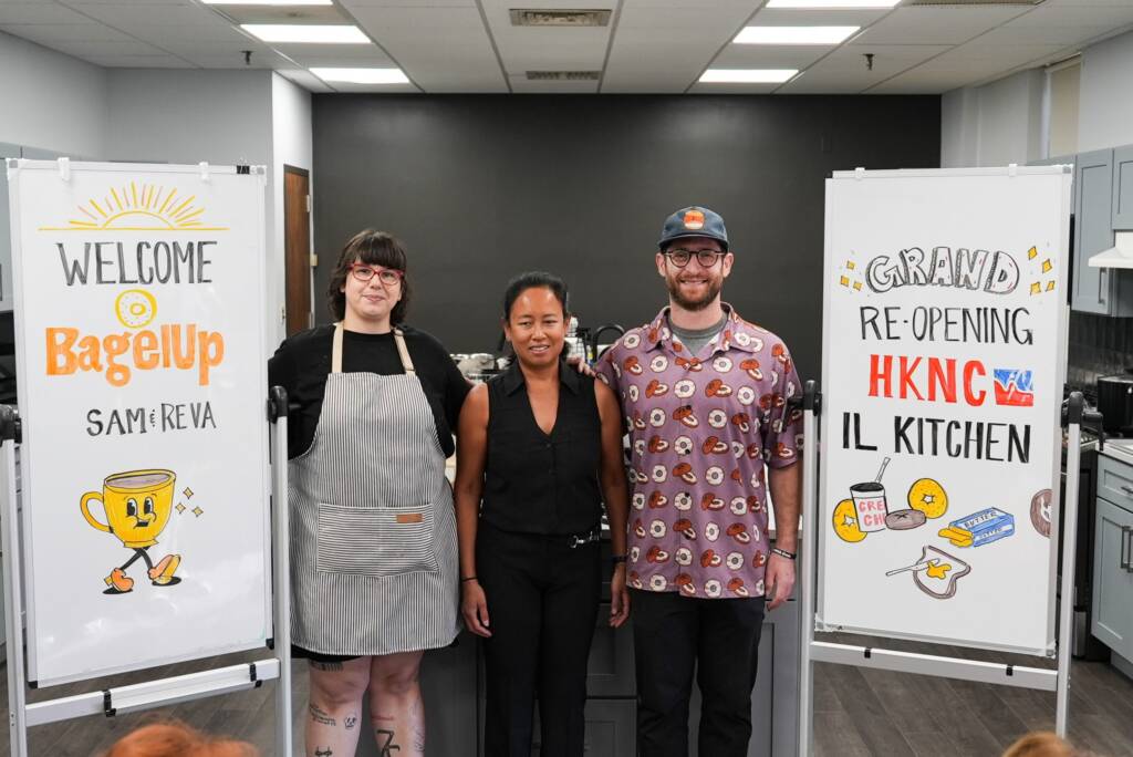 A group shot of Maricar along with Sam & Reva from BagelUp. Two vertical white boards stand alongside them. The white board on the left reads “Welcome BagelUp Sam & Reva” written in yellow and black.