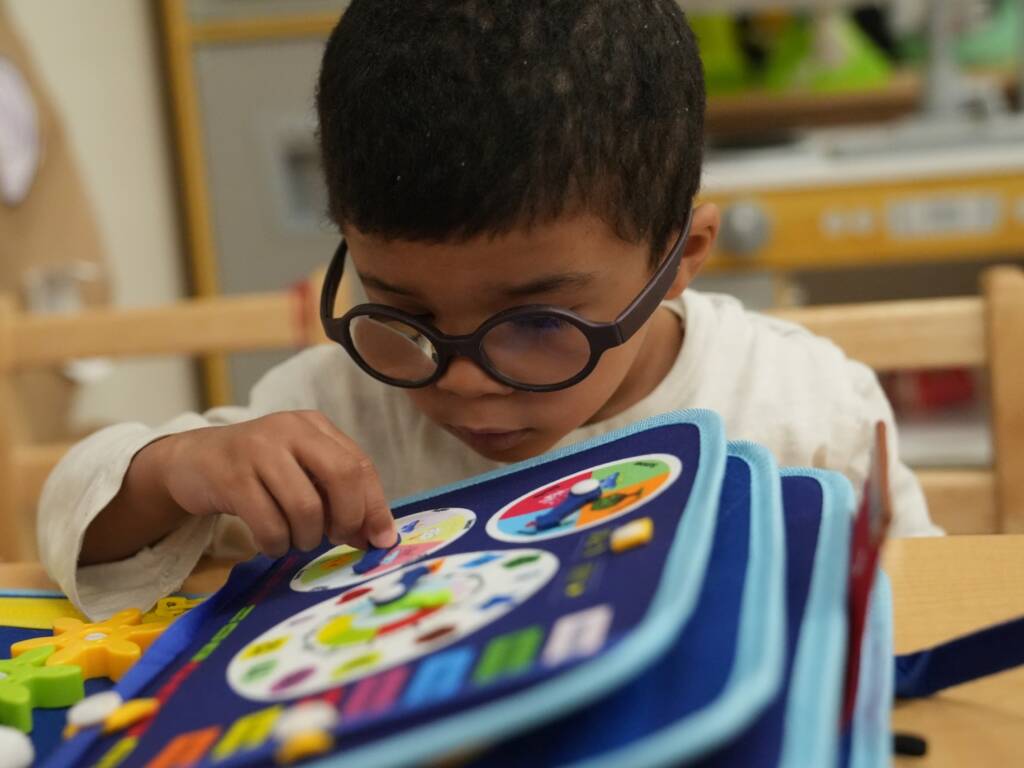A preschool boy with low vision interacts with a tactile activity book at the children's Learning Center.