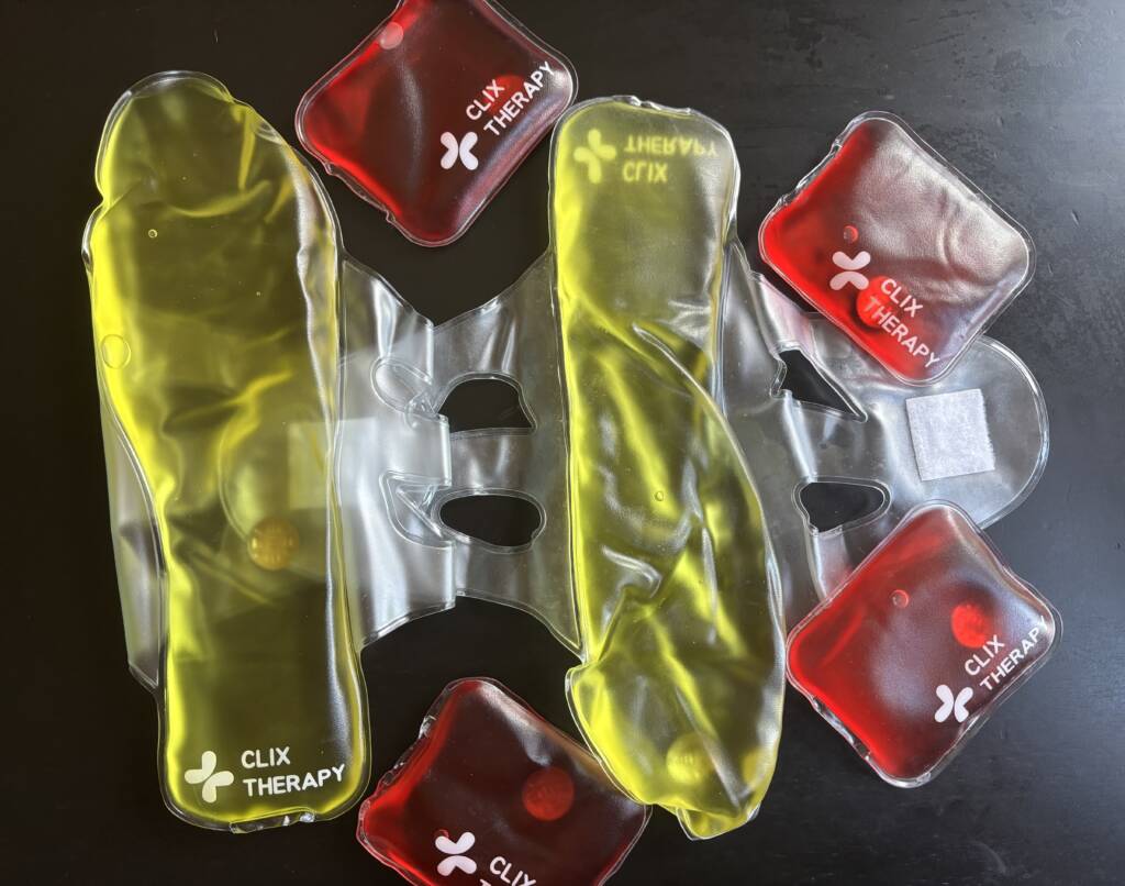 Various Clix Therapy reusable heat packs in yellow and red colors arranged on a dark surface.