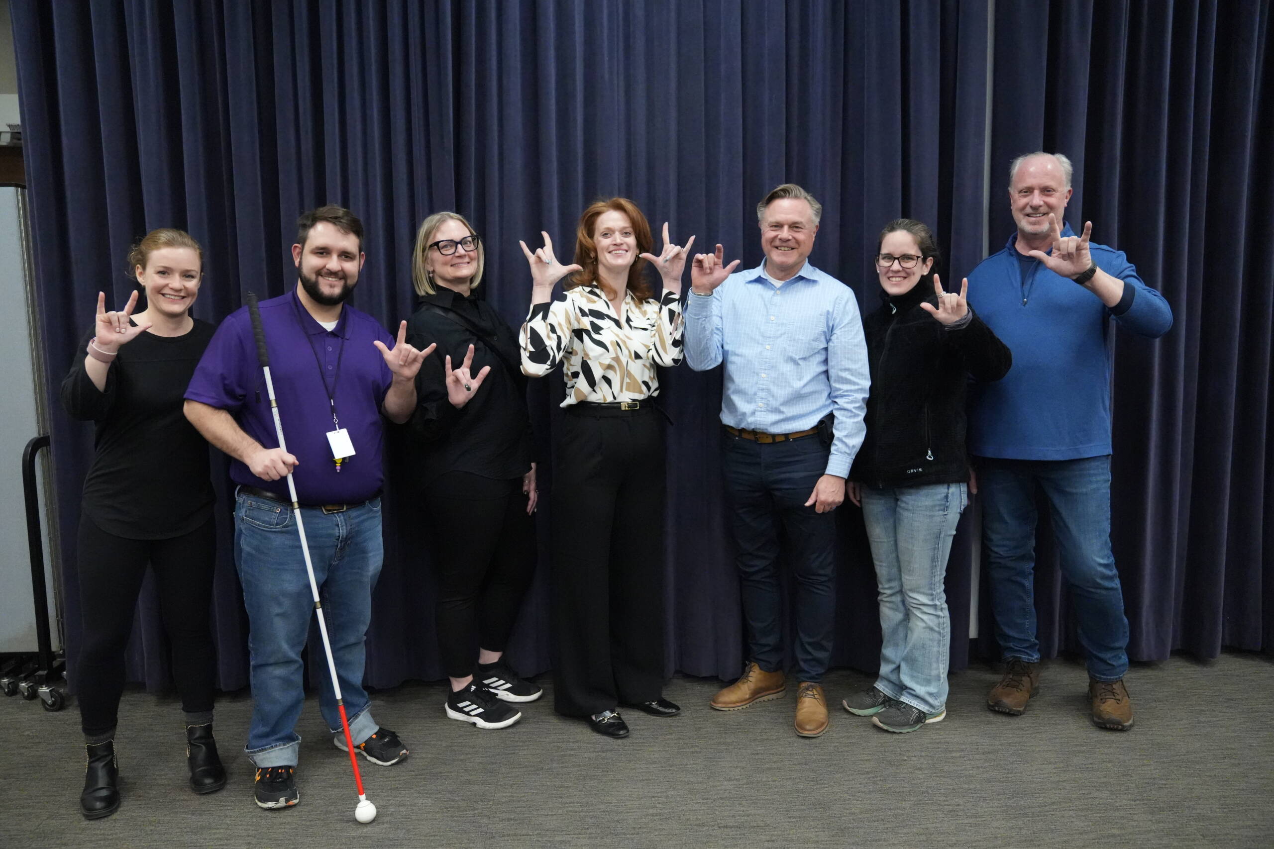 HKS staff and participants stand together with reps from Polara for a group photos.  they are all making the "I love you" sign in ASL.  