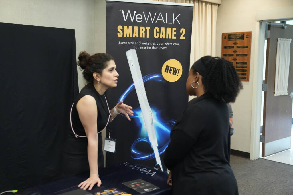 An attendee interacts with a representative at the WeWalk Smart Cane vendor table.