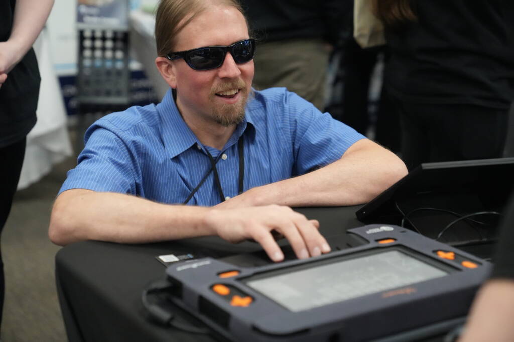 An attendee smiles while interacting with the Monarch braille display from American Printing House.