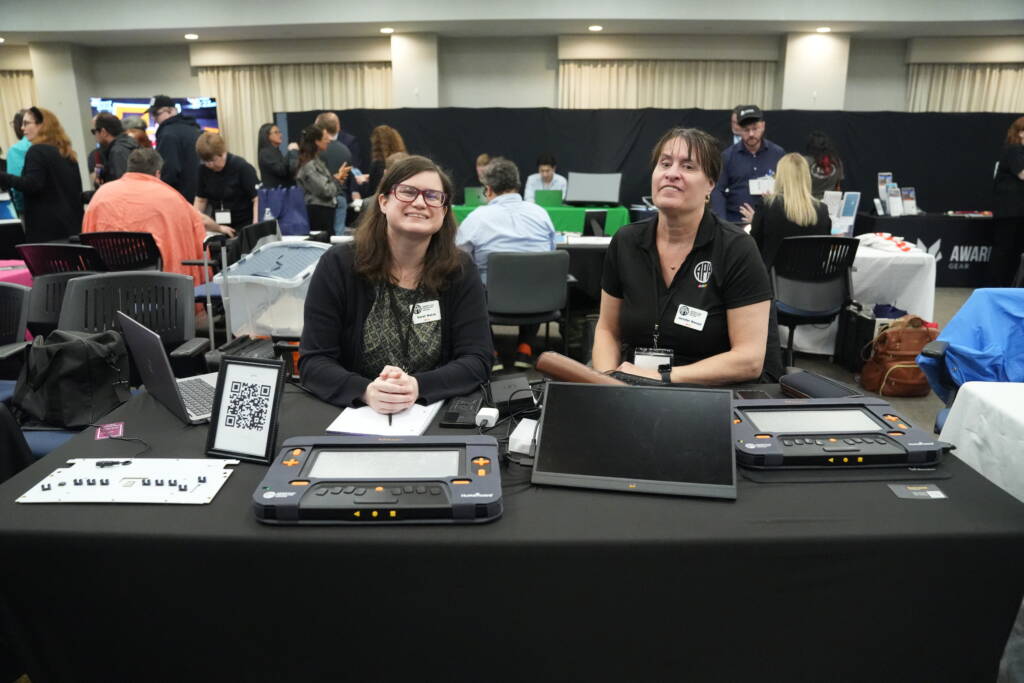 Representatives from American Printing House sit at their vendor table smiling for a photo.