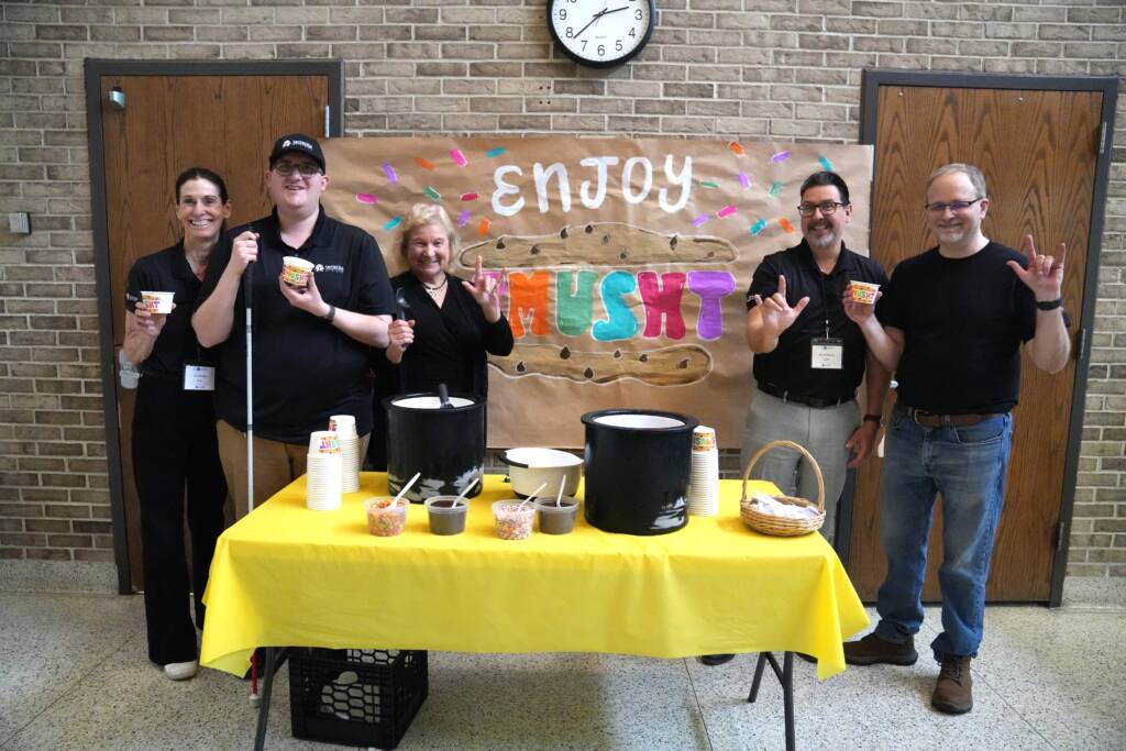 Liz Meade, Bryan Ward, Sue Ruzenski, John Filek and Jeff Kunkel stand at the ice cream table in front of a large hand-painted sign that reads "Enjoy Smusht"