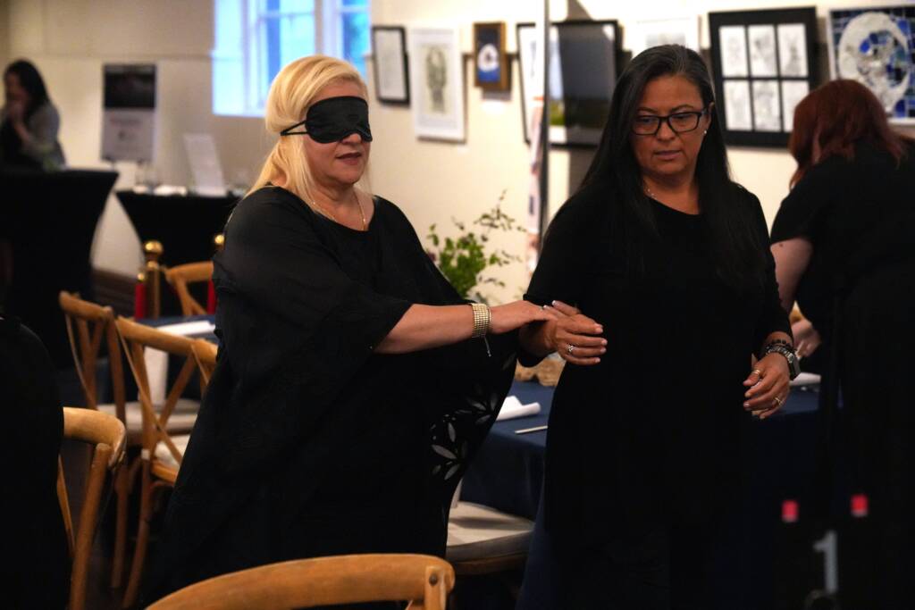 A female guest is guided under blindfold to her table by an HKS staff member.
