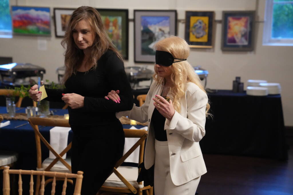 A female guest is guided under blindfold to her table by an HKS staff member.