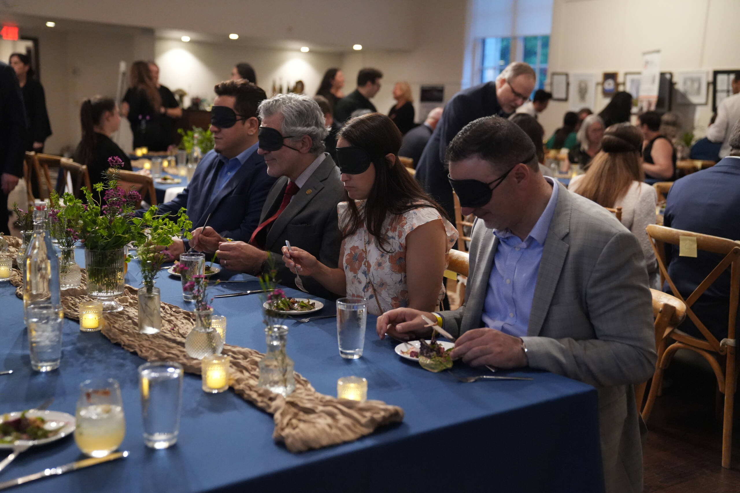 Four guest at Dining in the Dark are seated at a table wearing blindfolds and starting their salad course. 