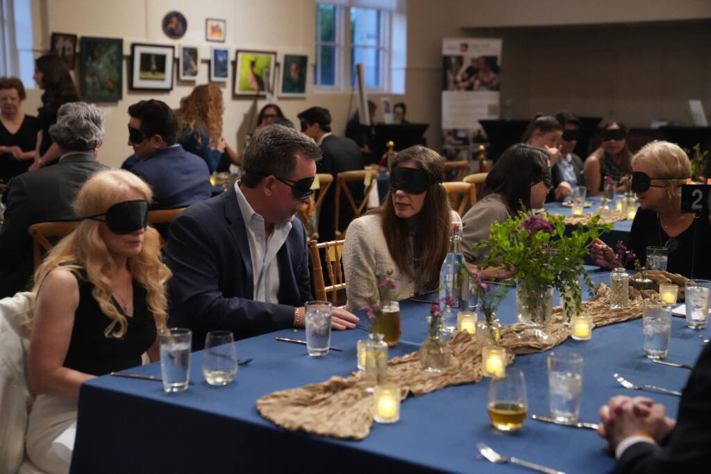 A group of guests are seated at their table wearing blindfolds and engaging in conversation. 
