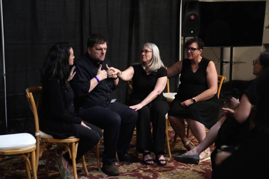 Ryan Odland and Ashley Benton having a discussion with interpreters by their side. Ryan and Ashley are communicating in tactile ASL.  