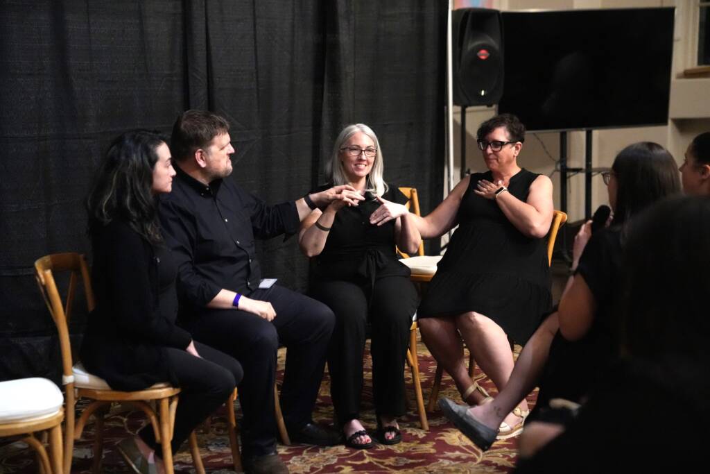 Ryan Odland and Ashley Benton having a discussion with interpreters by their side. Ryan and Ashley are communicating in tactile ASL.  