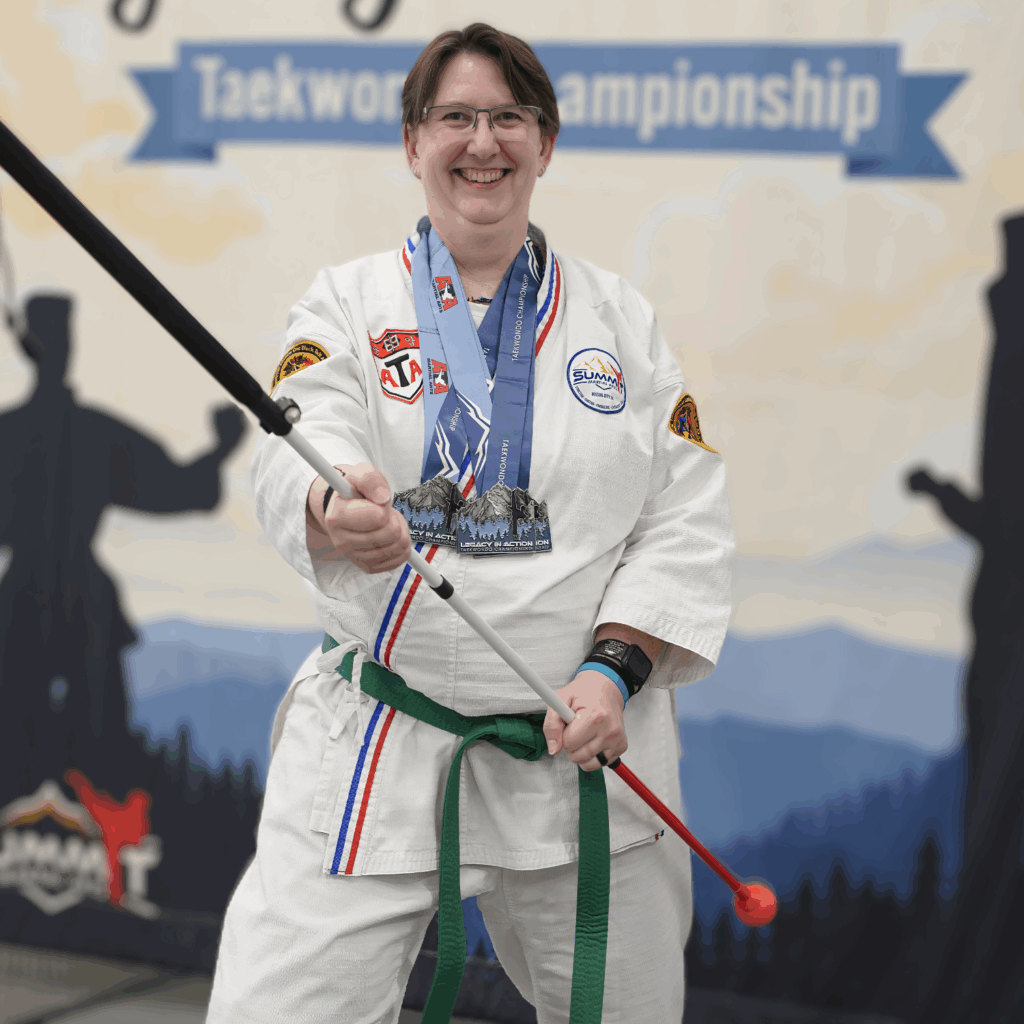 Laurie McBride in a white martial arts uniform holding a white cane in a taekwondo stance.