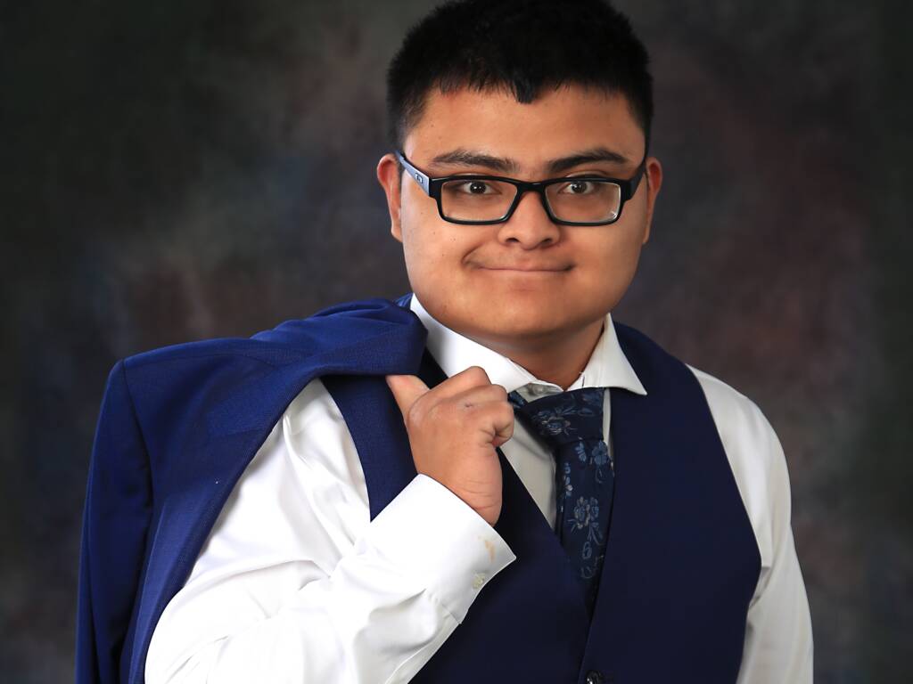 A DeafBlind young adult wearing a suite holding his jacket over his shoulder. 