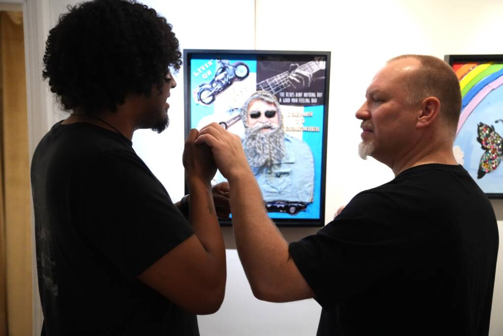 Two individuals engaged in tactile ASL communication standing in front of a piece of artwork on a wall.