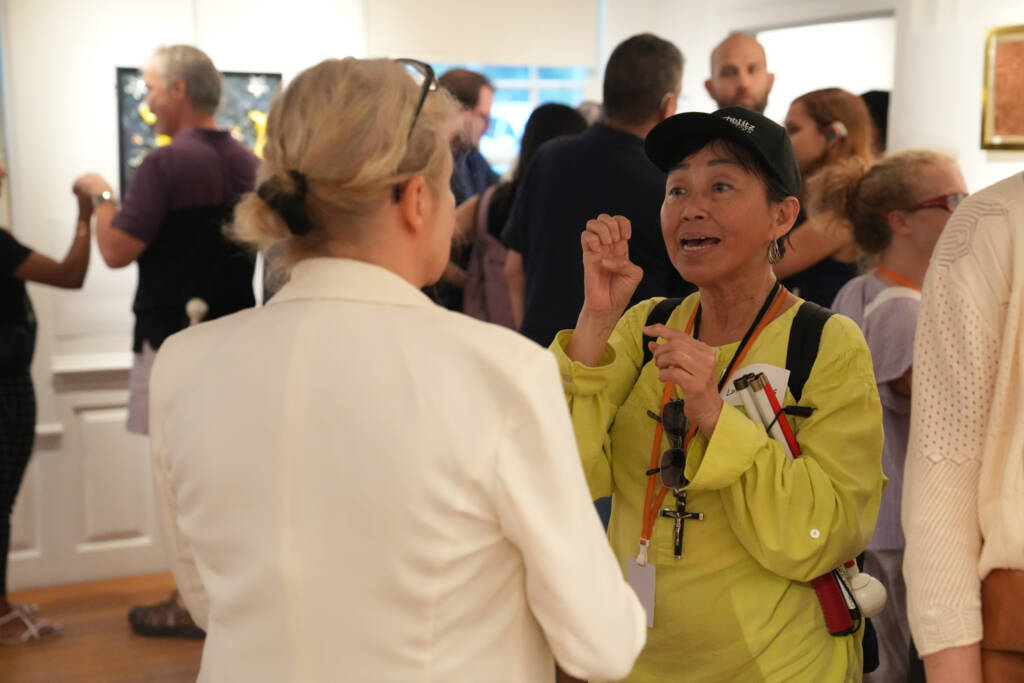A woman communicates in ASL with another woman during the exhibit reception. 