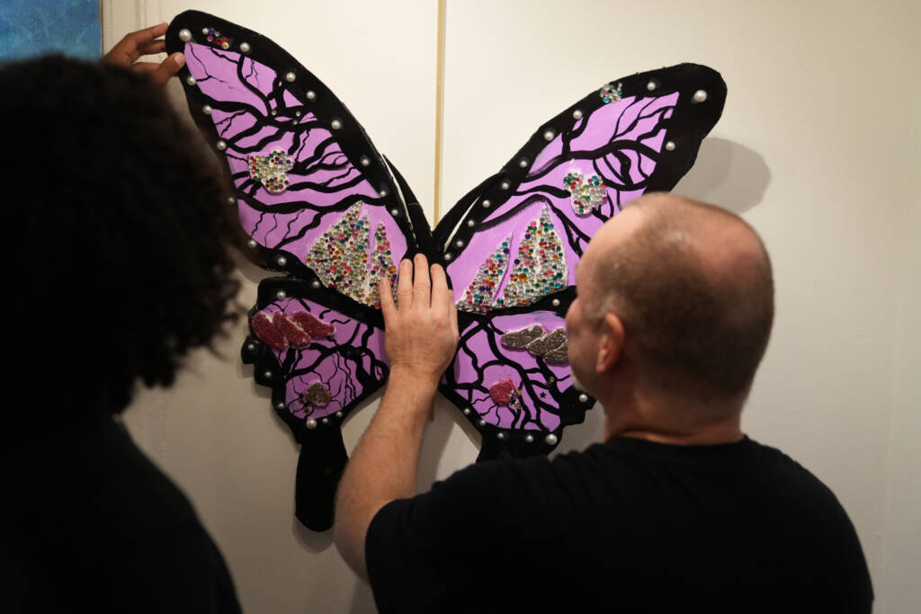 A man feels a piece of art on the wall.  the piece is a beautiful purple and black butterfly. 