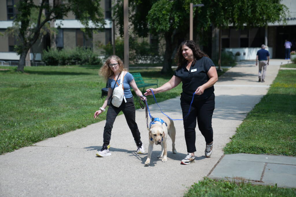 A female HKNC participant is guided on a Juno walk with a guide dog and trainer.