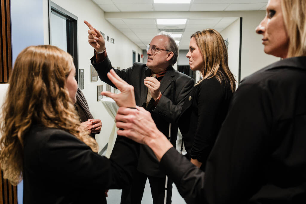 Attendees check out the new atrium in the background, while two individuals communicate in tactile sign language in the foreground