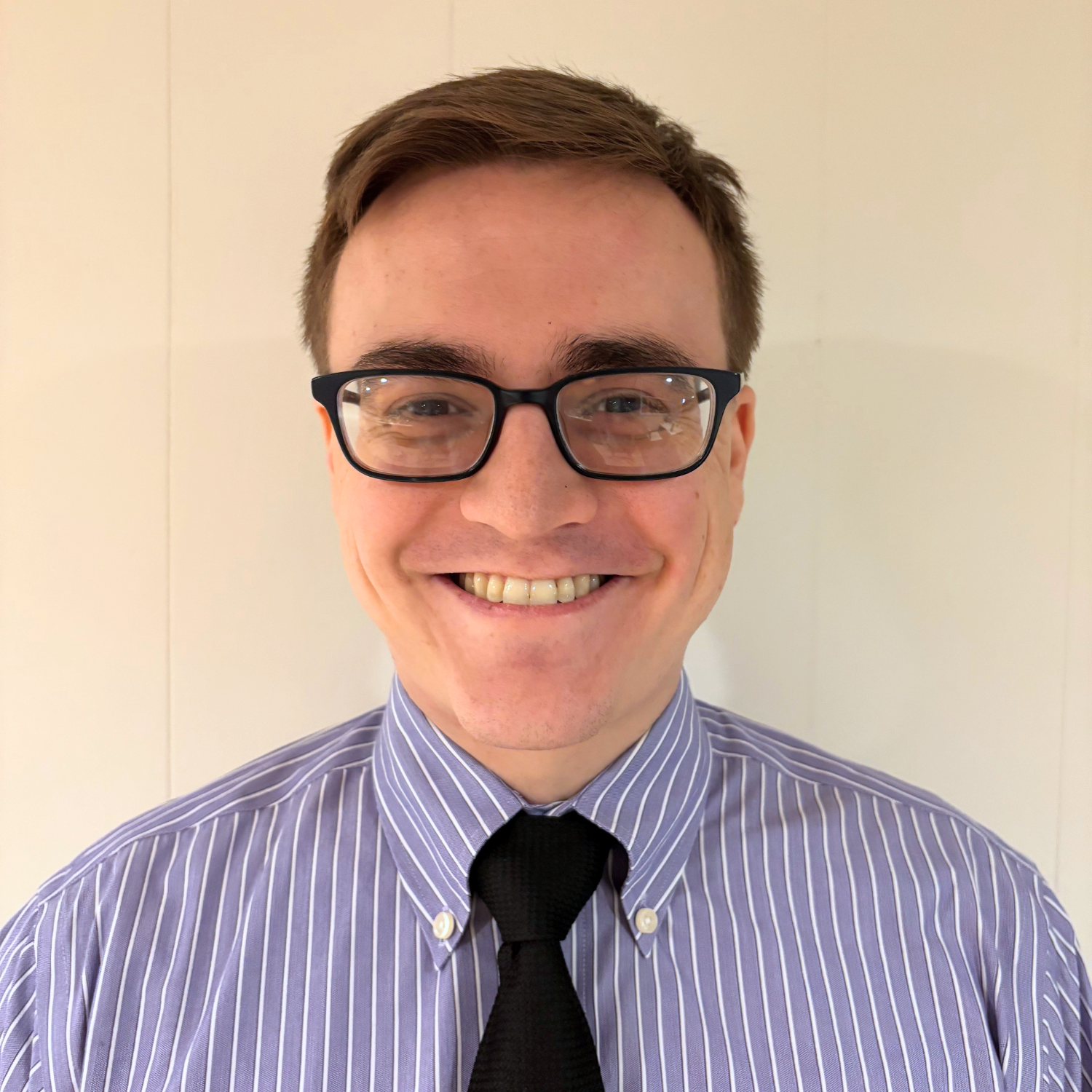 Headshot of a young adult professional wearing glasses and a shirt and tie.