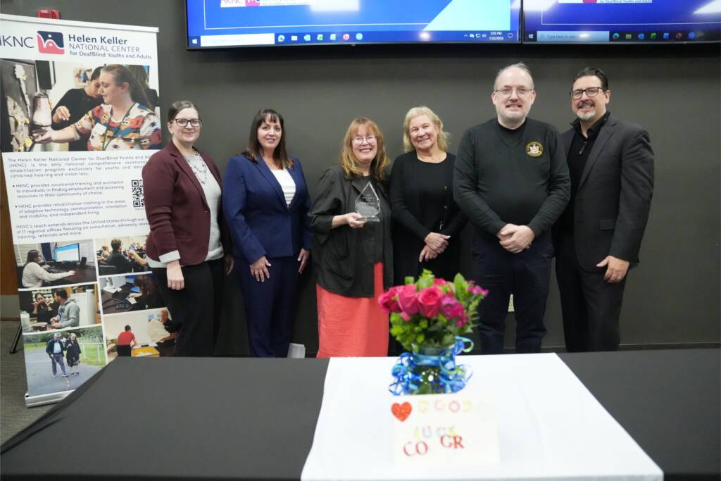 Laura Rocchio, center, holds her 2025 Code of Conduct Award alongside colleagues and Justice Center representatives. From left to right: Jessica Pidgeon (Chief of Staff, NYS Justice Center), Maria Lisi-Murray (Acting Executive Director, NYS Justice Center), Laura Rocchio (Director of Direct Services, Helen Keller National Center), Dr. Sue Ruzenski (CEO, Helen Keller Services), Chris Woodfill, and John Filek (Executive Director, Helen Keller National Center).