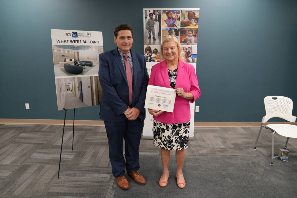 Dr. Susan Ruzenski, CEO of Helen Keller Services, stands with a Seth Squicciarino from State Senator Monica Martinez's office. Dr. Ruzenski holds a Certificate of Recognition presented during the groundbreaking ceremony.