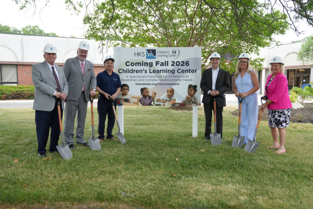 Six people in hard hats hold shovels in front of a sign announcing the Children's Learning Center coming Fall 2026 to Long Island.