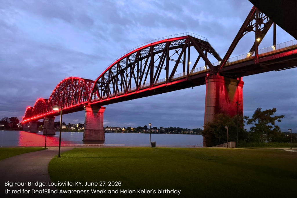 The Big Four Bridge in Louisville, Kentucky, illuminated in red at dusk on June 27, 2026, spanning the Ohio River, lit for DeafBlind Awareness Week and Helen Keller's birthday.