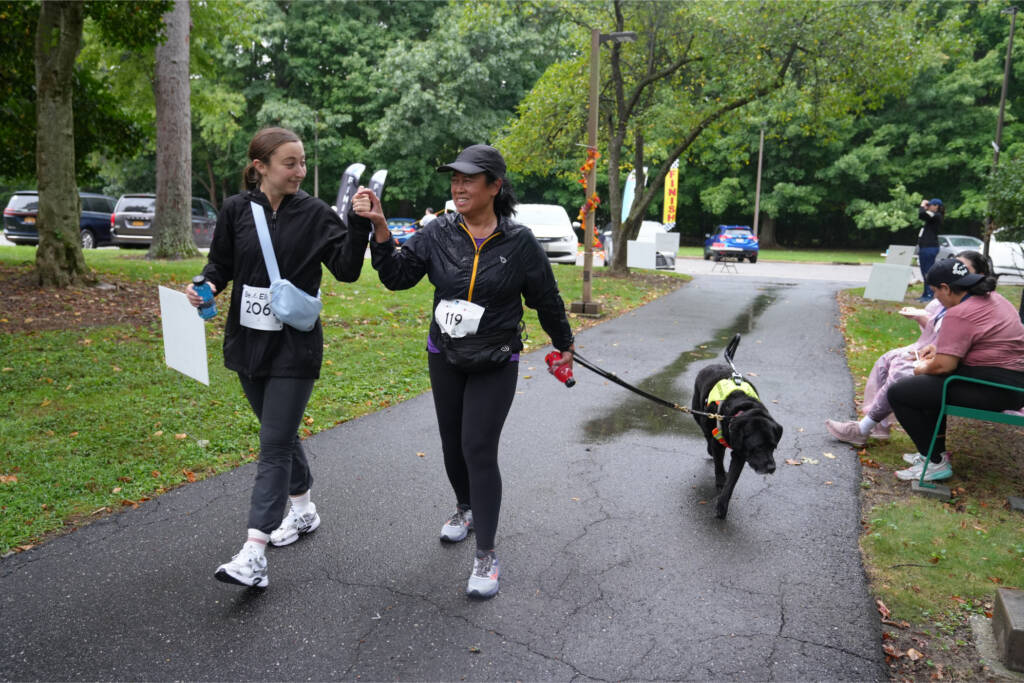 Maricar Marquez and her support service provider walk hands together in tactile communication as her guide dog Cliff leads the way after the race.
